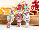 Three colorful nutcracker ornaments on a wooden surface with blurred lights and berries in the background.