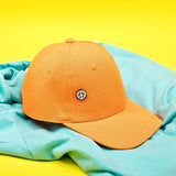 Peace pin on orange baseball cap on a turquoise top.