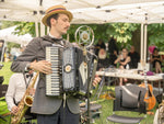 Man playing the accordion wearing a boater hat in front of an old microphone. 