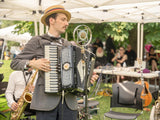 Man playing the accordion wearing a boater hat in front of an old microphone. 
