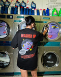 Person wearing a black t-shirt with colorful graphics and text in a laundromat.