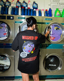 Person wearing a black t-shirt with colorful graphics and text in a laundromat.
