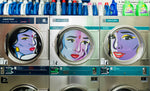 Laundry machines with artistic faces on their doors in a laundromat.