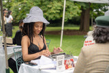 Woman sitting at a table outdoors with a typewriter, engaged in conversation.