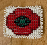 Beaded design of a red poppy with a green and black center on a wooden surface