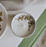 Candle in a metal container with cedar on the surface.
