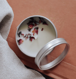 Candle in a metal tin with dried flowers on a wooden surface