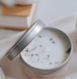 Candle in a metal container with sage on the surface.