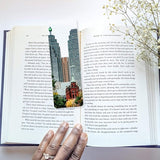 Open book with a cityscape bookmark and a hand holding the book.