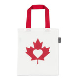 White tote bag with red maple leaf design with a white heart in the middle and red handle on a white background