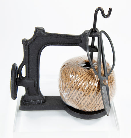 Cast iron shaped like a vintage sewing machine holds a ball of twine and a pair of scissors. 