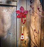 Maple leaf shaped iron hook mounted on fence with key and keychain hanging from hook.